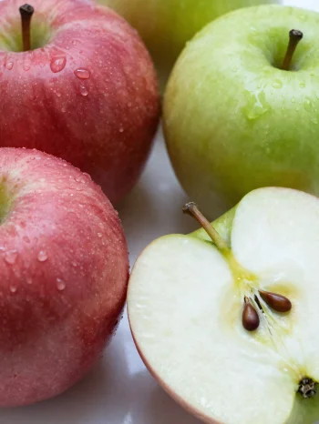 Färska röda och gröna äpplen på en skärbräda, skivade och hela, med äppeljuice