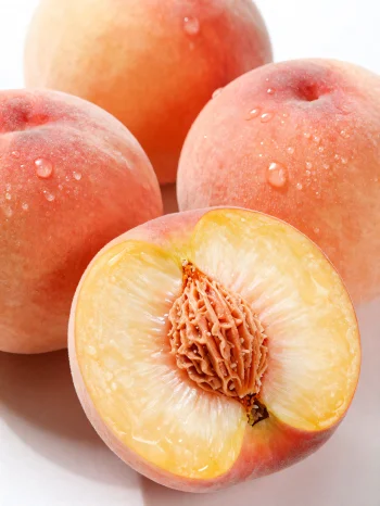 Hela och skivade persikor på ett träbord, bredvid ett glas persikojuice