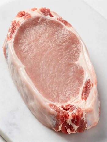 Färska bitar av ljust kalvkött med kryddor på en skärbräda av trä