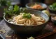 Pho med sesamolja serverad i skål med sesamolja, risnudlar, färsk koriander och limeskivor